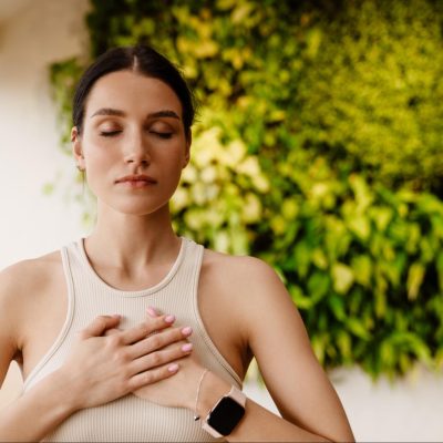 Young white woman demonstrating how to practice mindfulness, with her hands resting gently on her heart while controlling her breath.