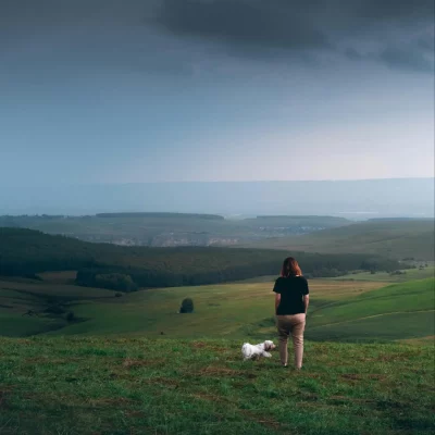 Woman contemplates unhealthy relationship patterns on a walk with her dog as the clouds roll into her scenic overlook.