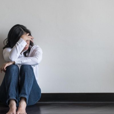 Distraught young woman sitting on the floor, holding her head and wondering, "What is a panic attack vs anxiety attack?"